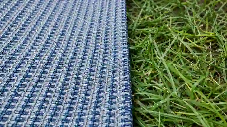 Close-up of a breathable blue woven awning carpet edge on green grass.