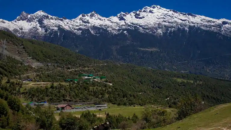 Snow-capped Himalayan mountain peaks and a green valley under a clear blue sky on the route to Tawang.