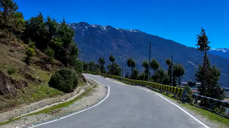Smooth asphalt mountain road with yellow safety barriers winding through Himalayan hills toward Tawang.