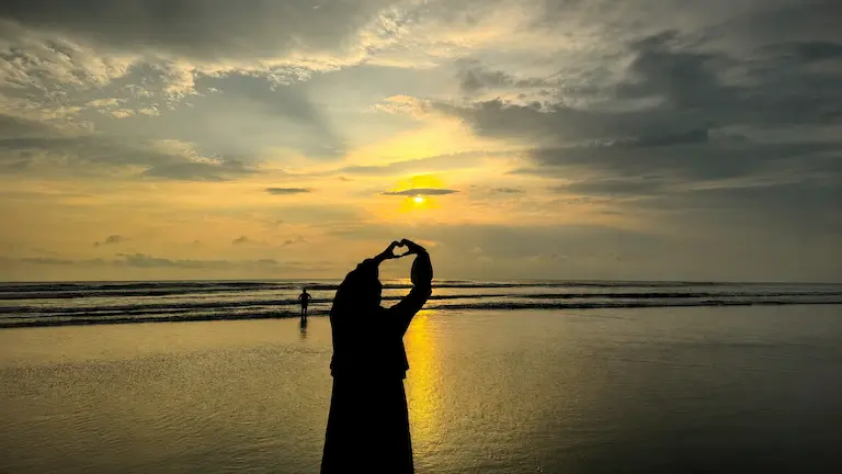 Silhouette of a person making a heart shape with their hands during a golden twilight at Lal Kakra Beach.